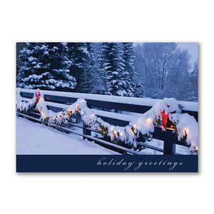 Holiday greetings card featuring a snow-covered fence decorated with garland lights and red bows