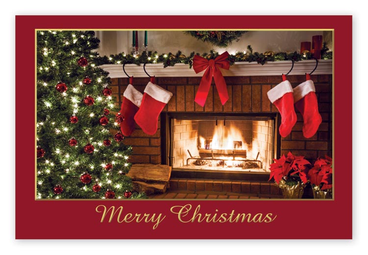 Christmas postcard showing a lit fireplace behind a Christmas tree and four stockings.